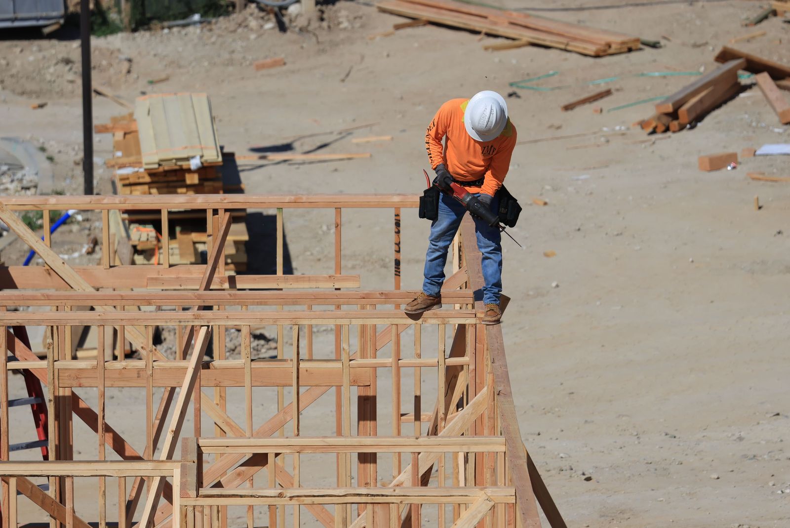 Construction worker in a hard hat using a drill on wooden house framing at a residential site