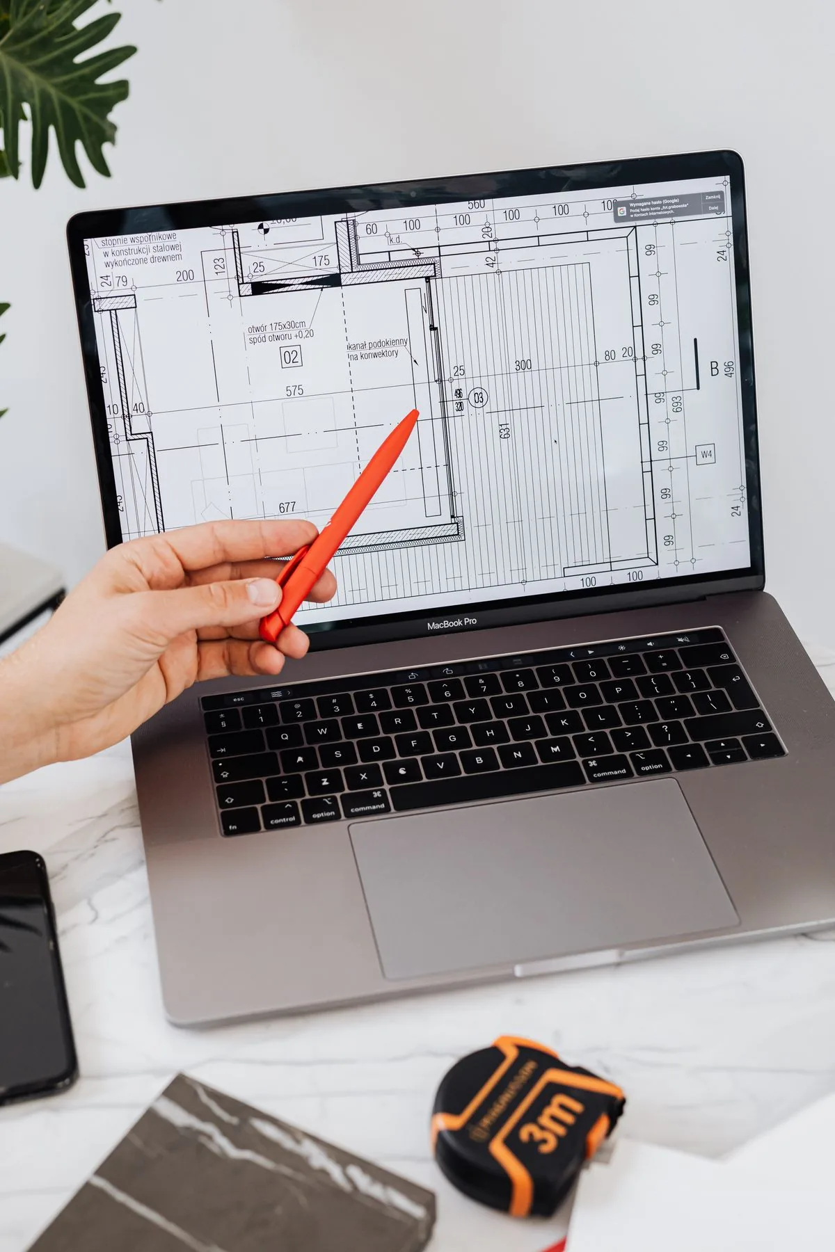 Hand marking up plans on a laptop with a tape measure on the desk