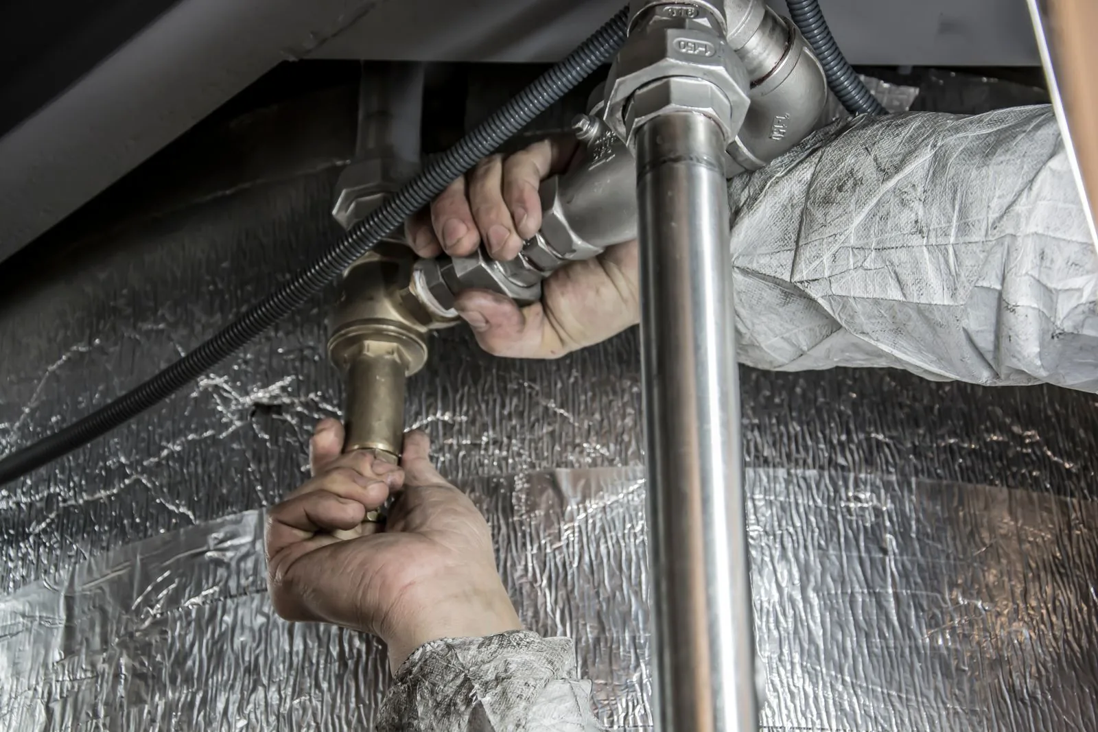 Plumber's hands tightening a fitting on pipes under a sink