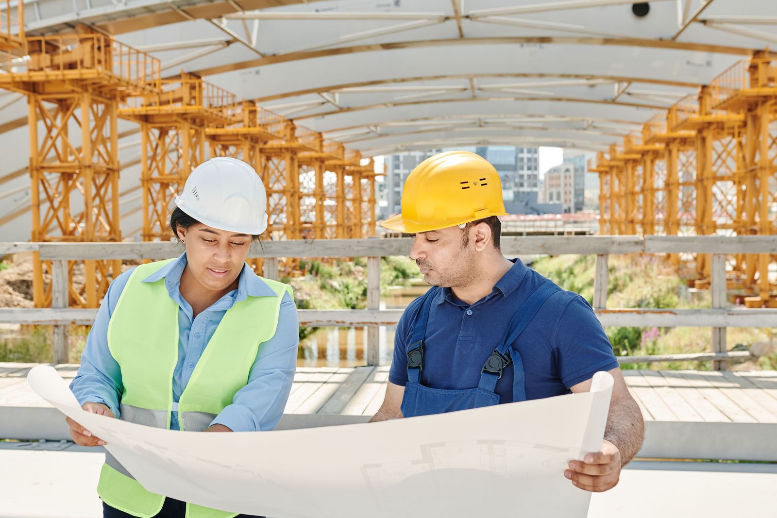 Two construction professionals in safety gear reviewing a blueprint on site